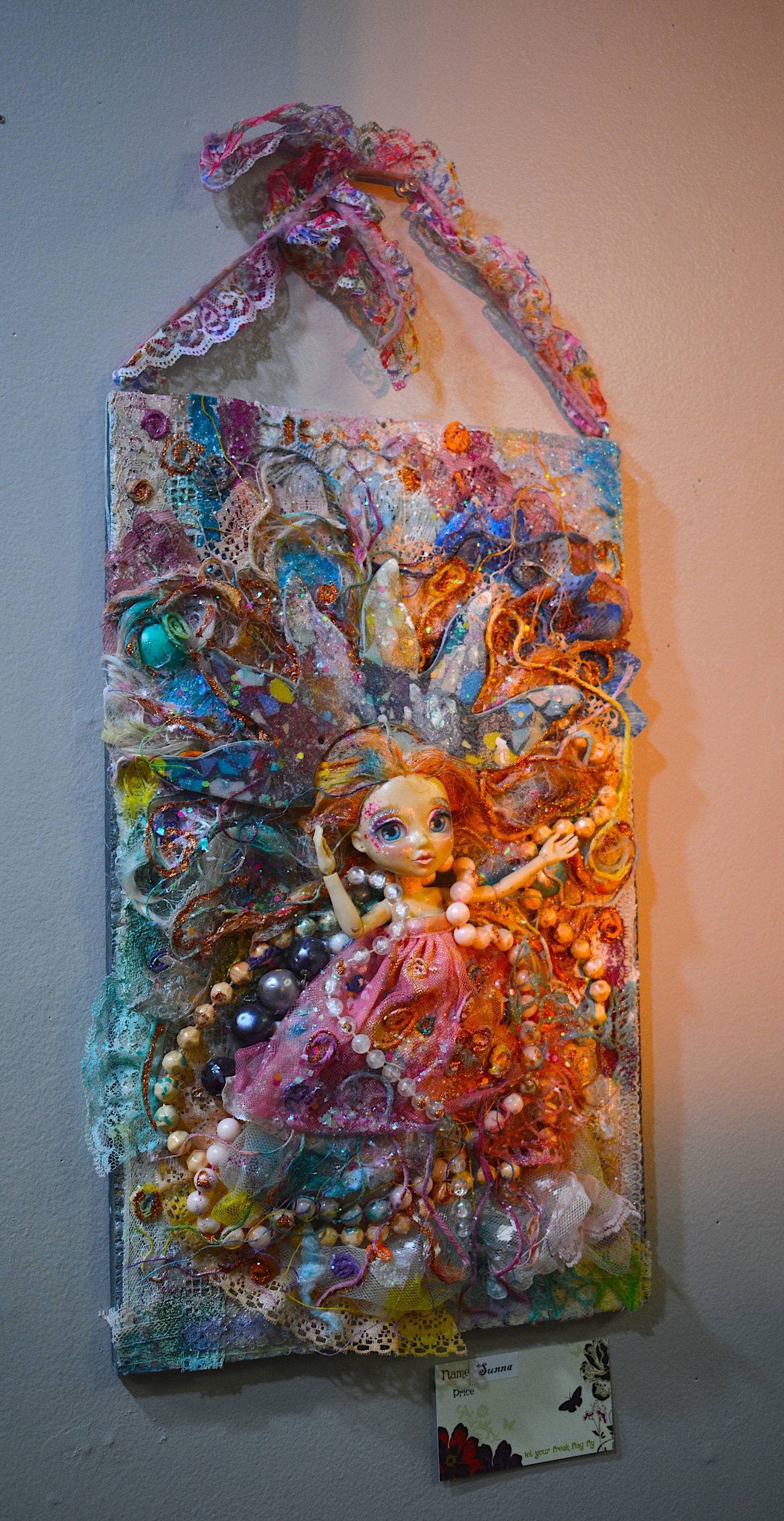 A doll is surrounded by beads and paint, turning a design featuring dozens of items into an intricate collage.