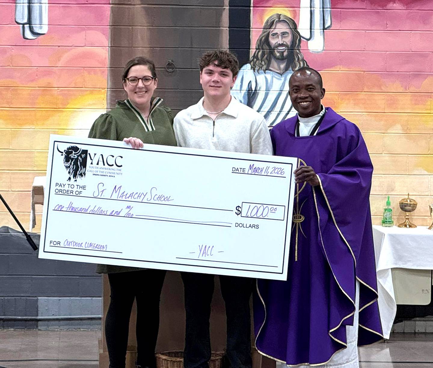 YACC participant and St. Malachy eighth grader Sam Anderson presents a check for $1,000 to St. Malachy for the outdoor classroom. From left, Brea Ramsey, Anderson, Fr. Patrick Amedeka.