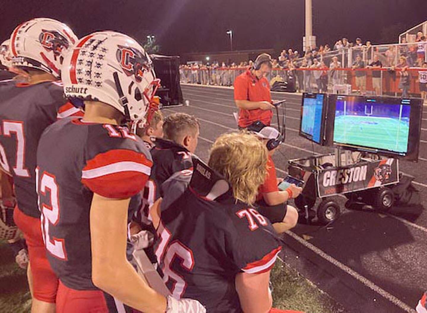 Offensive coordinator Garrison Carter meets with the offensive unit during Friday's homecoming game, viewing previous plays via the HUDL system on the video monitors connected to the staff's iPads. Creston has separate offensive and defensive platoons this season.