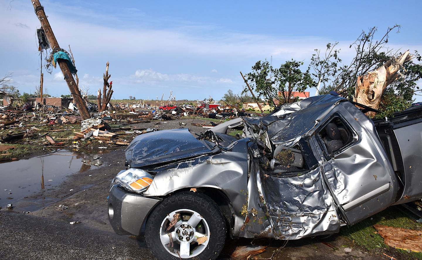A truck is crushed and completely warped in the aftermath of the tornado's wrath, the metal structure collapsed from debris.