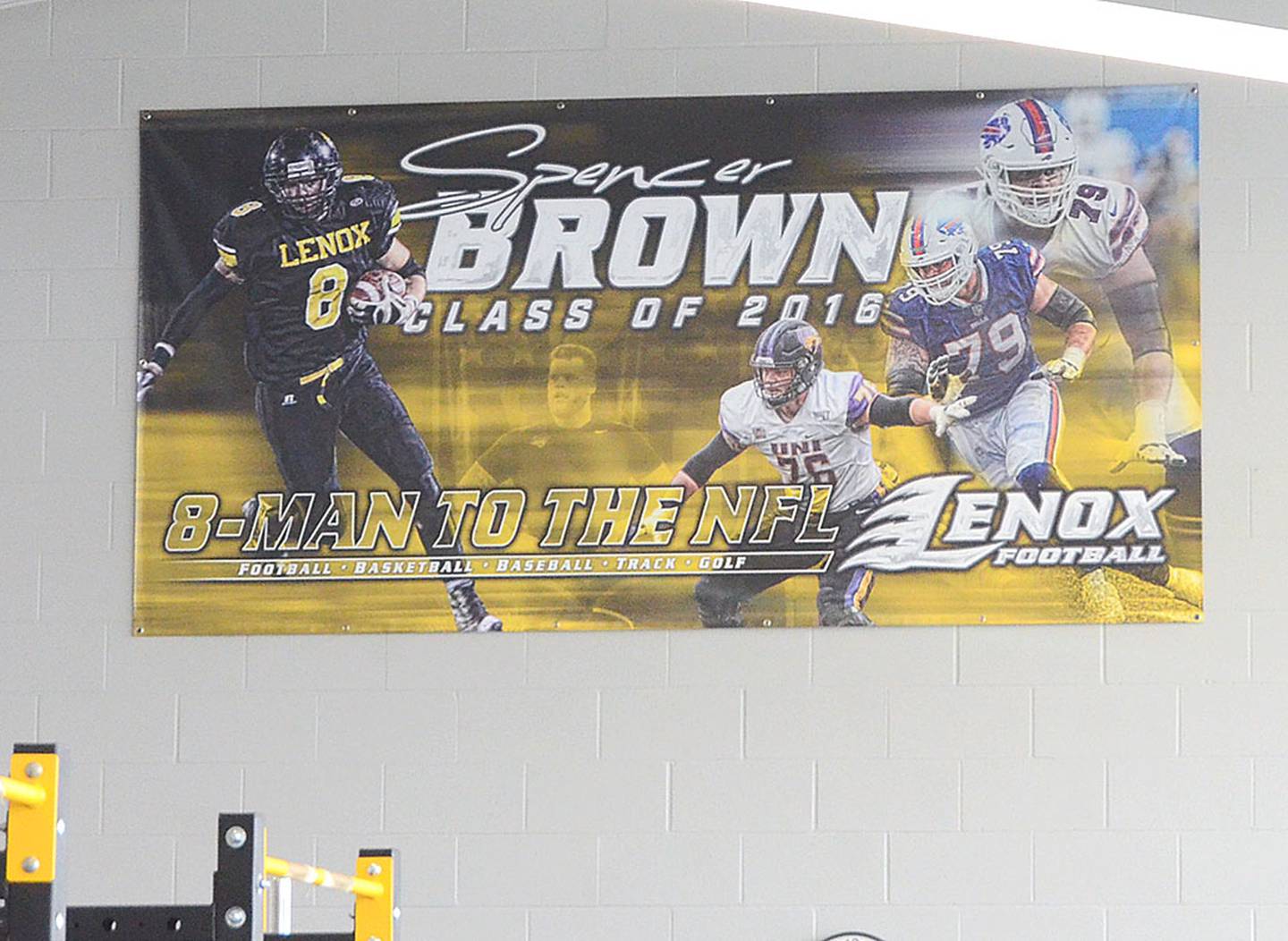 A poster showing Spencer Brown as a player at Lenox High School, University of Northern Iowa and with the Buffalo Bills hangs on the wall of the school's weight room, where Brown met with current players Friday.