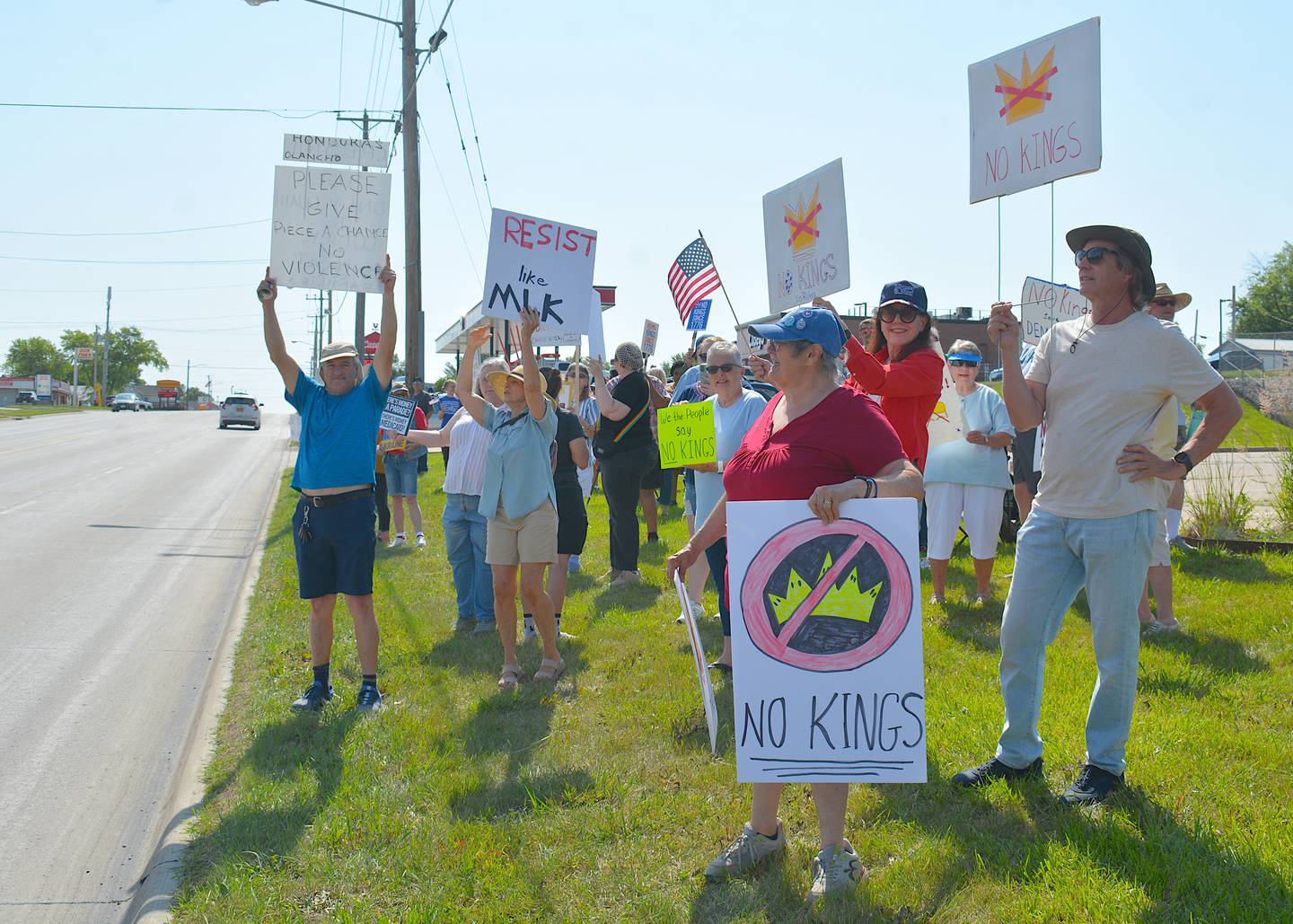 Protesters wave their signs to passing motorists. Some signs read "No Kings."