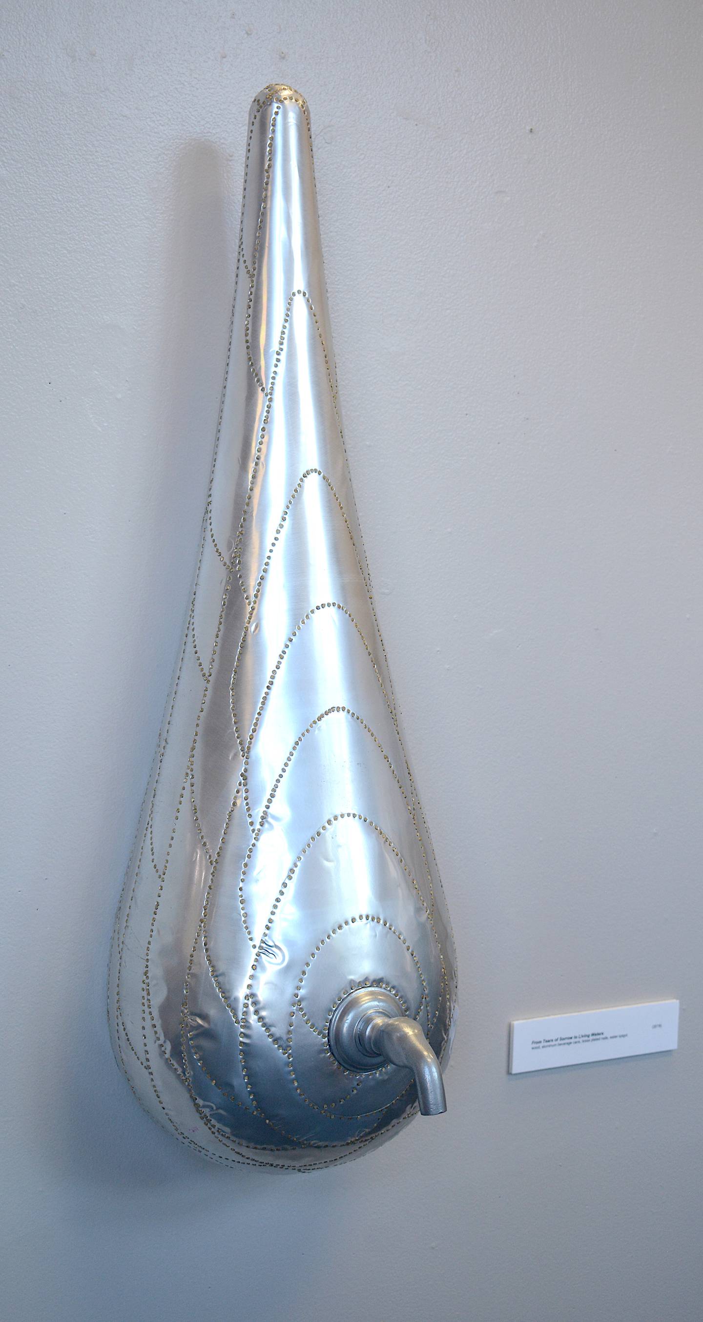 A sculpture called "From Tears of Sorrow to Lining Waters" by Patrick Luber. The aluminum teardrop has a metal faucet jutting out of it. Each sculpture in Luber's exhibit is made primarily out of aluminum cans.