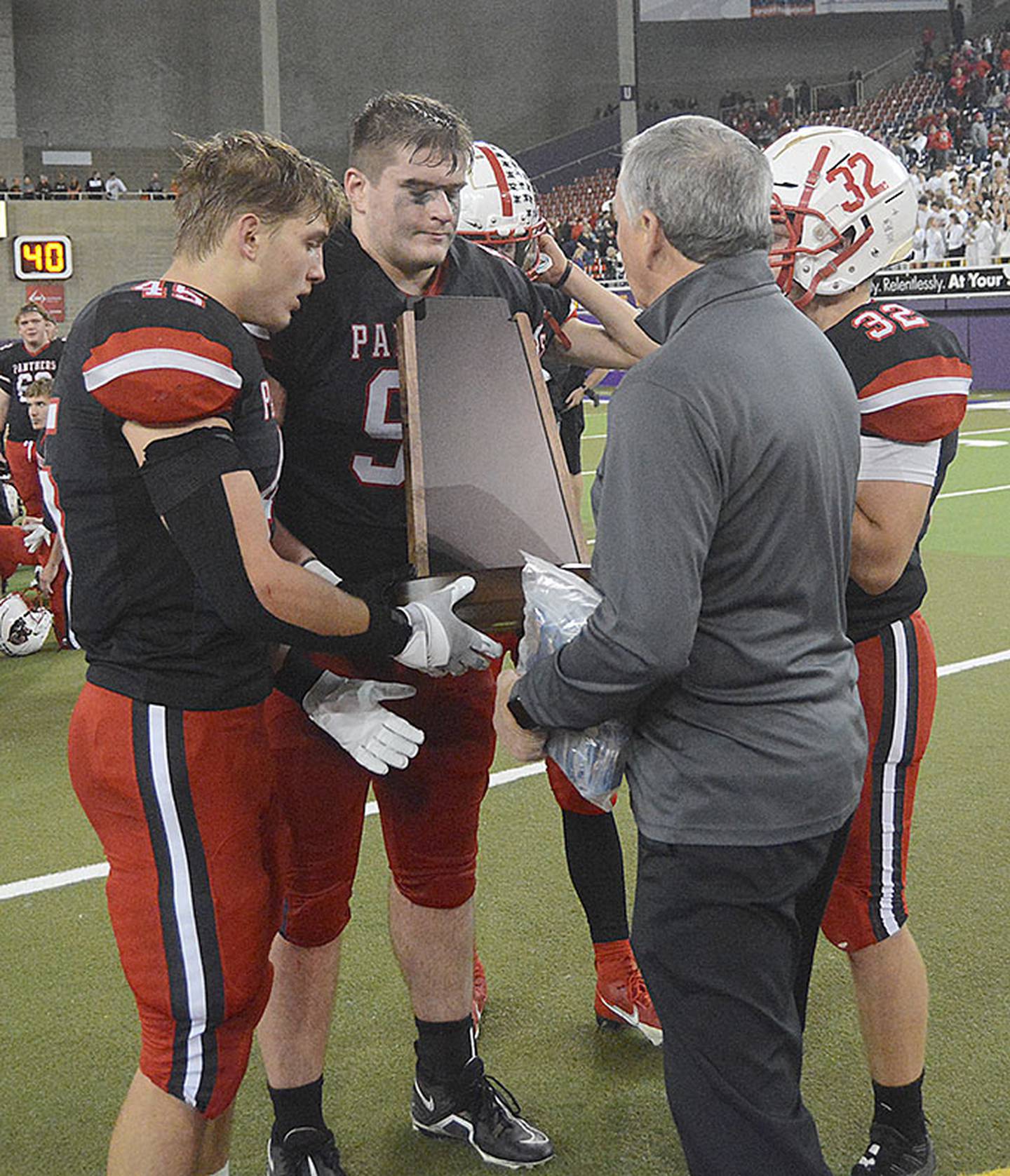 A representative of the Iowa High School Athletic Association presents the Class 3A semifinals trophy to Creston captains, from left, Brennan Hayes, Max Chapman, Cael Turner and Austin Evans.