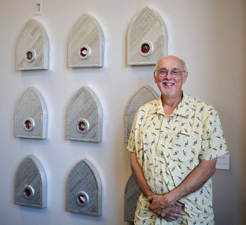 Patrick Luber alongside his newest sculpture, titled "Reliquaries for Liminal Objects," a collection of nine similar pieces. Each sculpture has a small hole where an object is placed. The center sculpture holds a trimmed dollar bill, and is titled "Object of Values and Worthlessness."