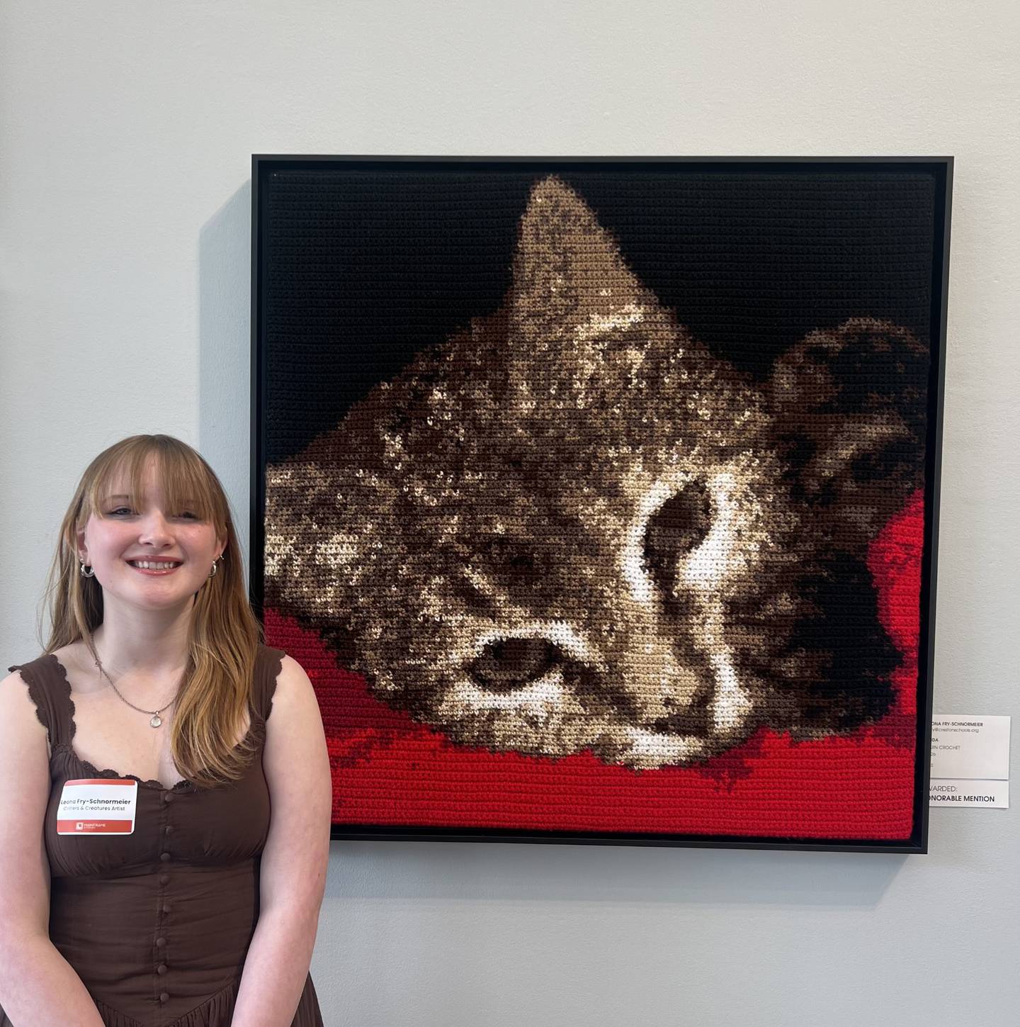 Leona alongside her artwork featured at Mainframe Studios. The family cat, Frida, is captured in the tapestry.