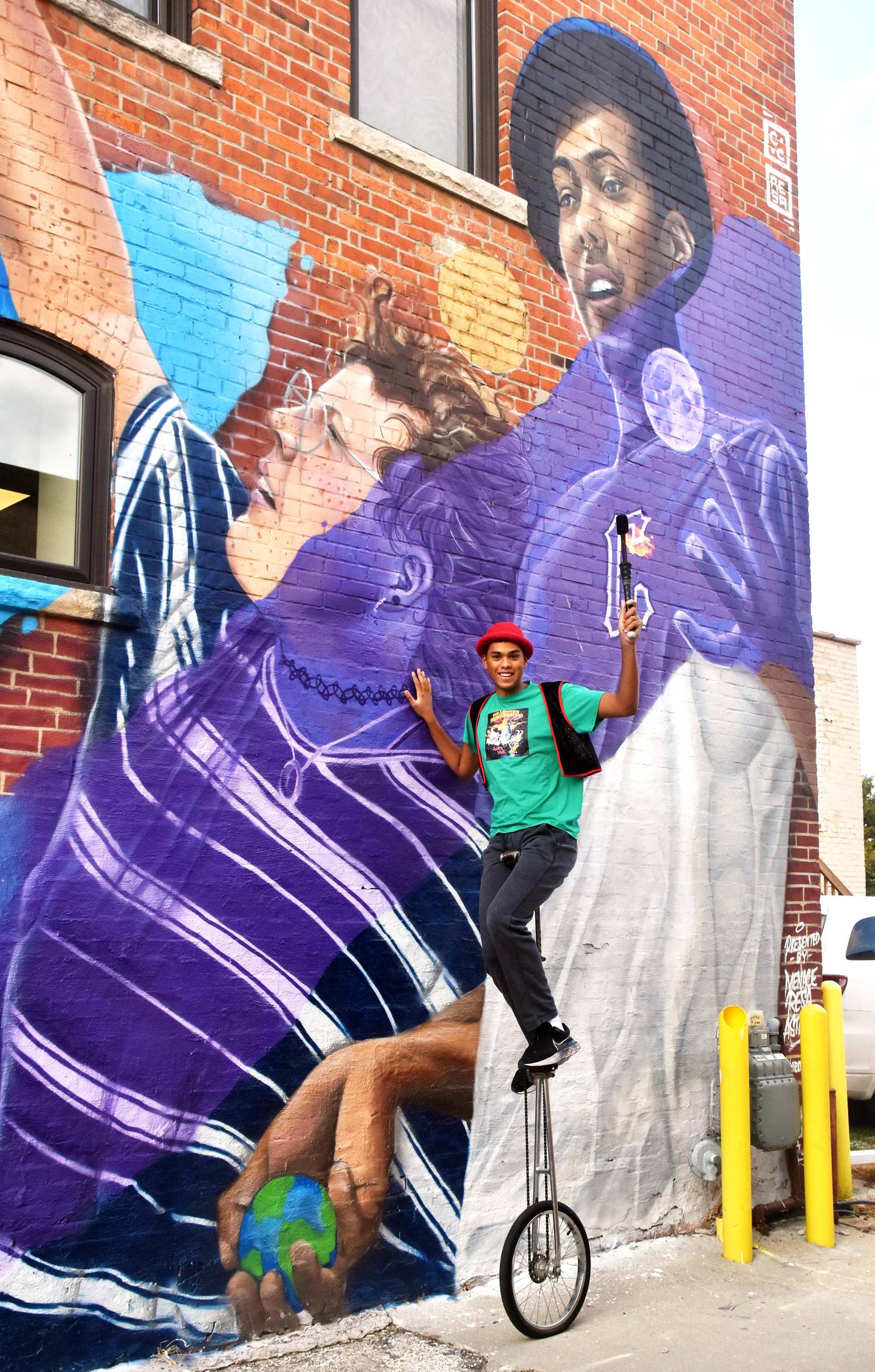 Raltson poses on a 6-foot unicycle in front of the mural he’s depicted in. The INSPIRE mural was painted by Menace and Resa featuring Astroe.