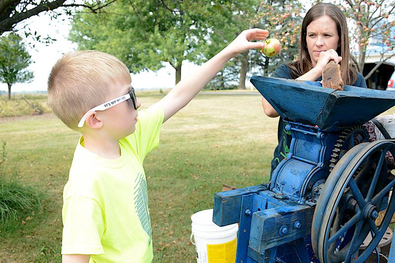 Judah Hamer adds apples to the crusher, ran by his mother Brenda Hamer, during an apple cider making event at Larry Joe Vandewater's farm recently northeast of Greenfield.