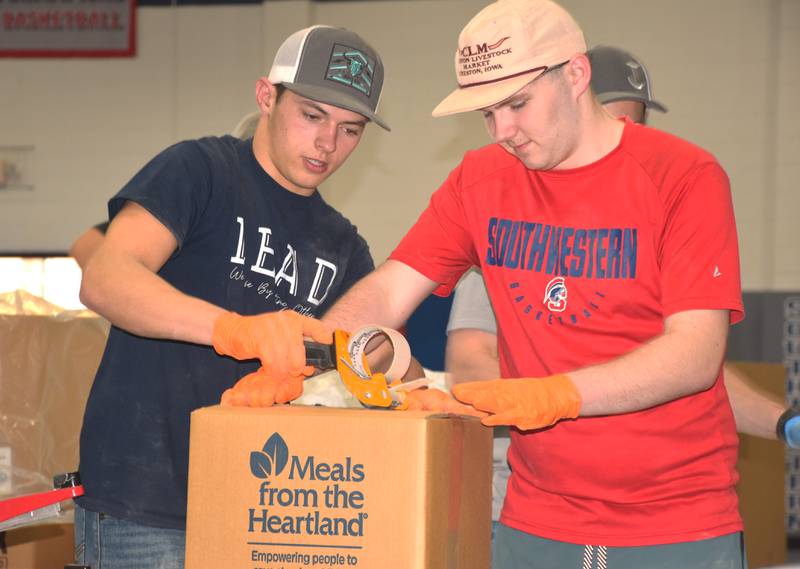 Lane Travis and Nate Carroll package a box of 36 meals Wednesday at the annual Meals for the Heartland volunteer event.
