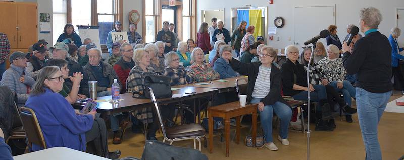 A crowd arrived at the Restored Depot to discuss their concerns with the federal government. Pat Shipley introduces the event. A Ukrainian flag is hung near the exit of the room.