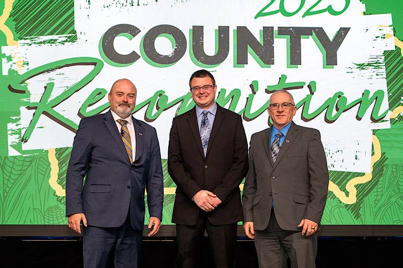 Adair County Farm Bureau President Clark Dolch (center) accepts congratulations for Adair County Farm Bureau being named an “Outstanding County Farm Bureau” from IFBF President Brent Johnson and District 9 Farm Bureau Director Will Frazee, on stage at the IFBF Annual Meeting.
