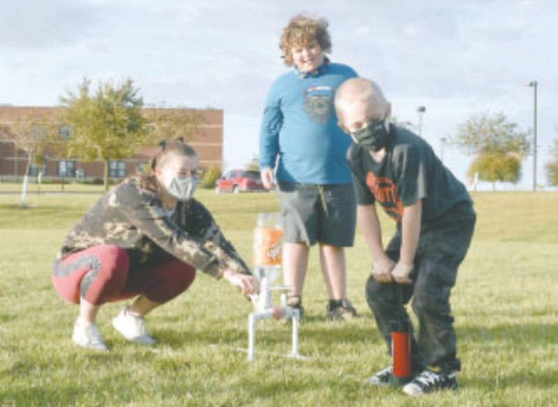 Charlie Anderson watches as Boy Scout volunteer Abbi Hood steadies a plastic bottle rocket on a launch pad made of PVC pipe as Henry Miller builds pressure for the launch using a bicycle pump Tuesday evening near Creston Community Middle School.
