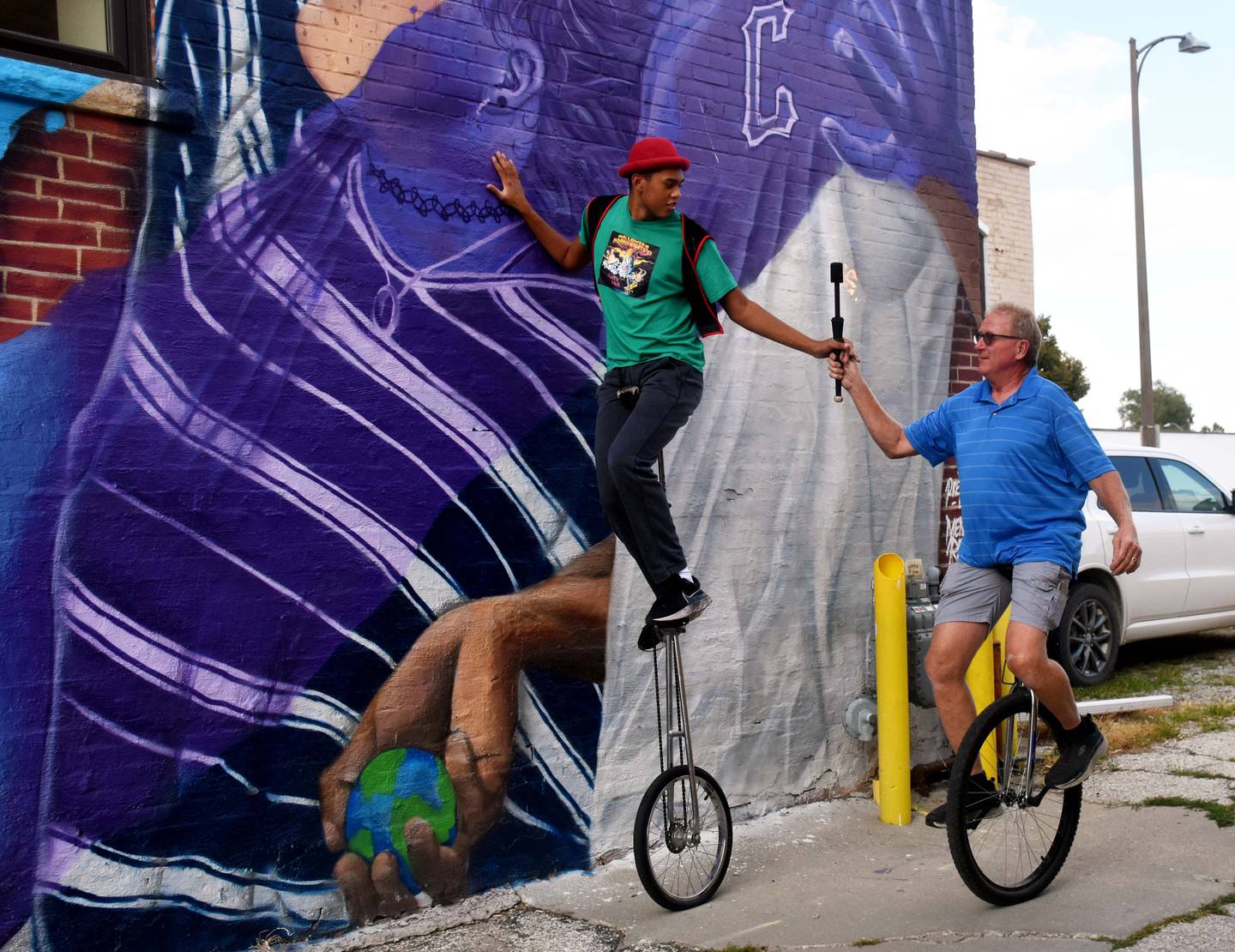 Jon Carroll, right, passes the torch to Isaac Ralston after nearly 30 years of riding the  6-foot unicycle.