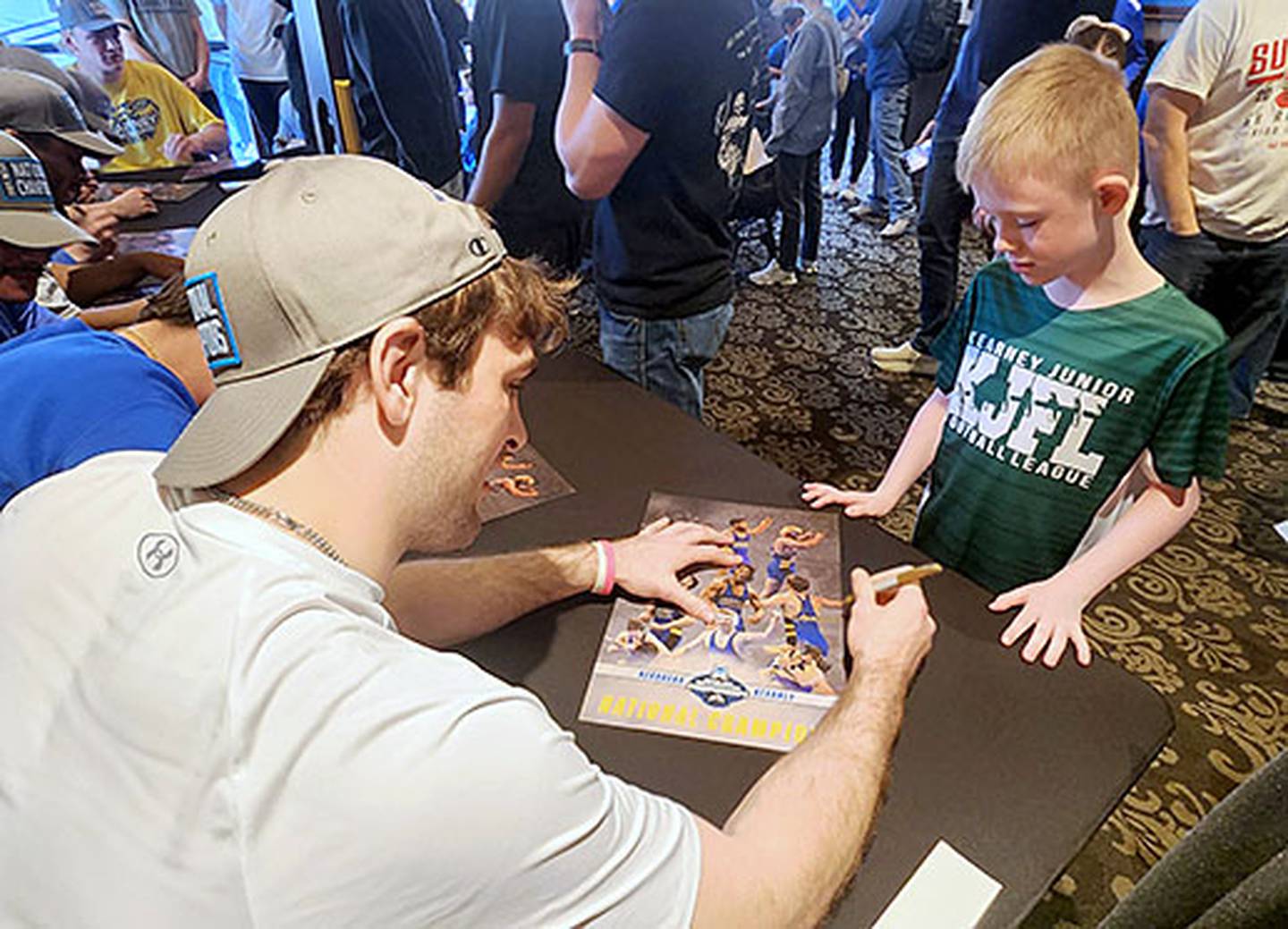 Jackson Kinsella signs an autograph on a Nebraska-Kearney championship poster for a young fan at the reception held Sunday at World Theatre in Kearney.