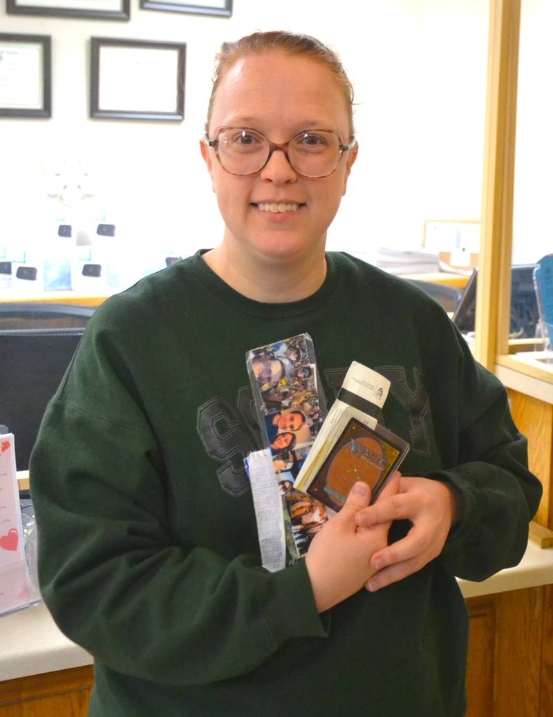 Library Programming Specialist Heather Pingree poses with a handfull of the items left in books over the years, including personalized bookmarks, a ticket to the Pearl Harbor Memorial and even a Magic the Gathering card.