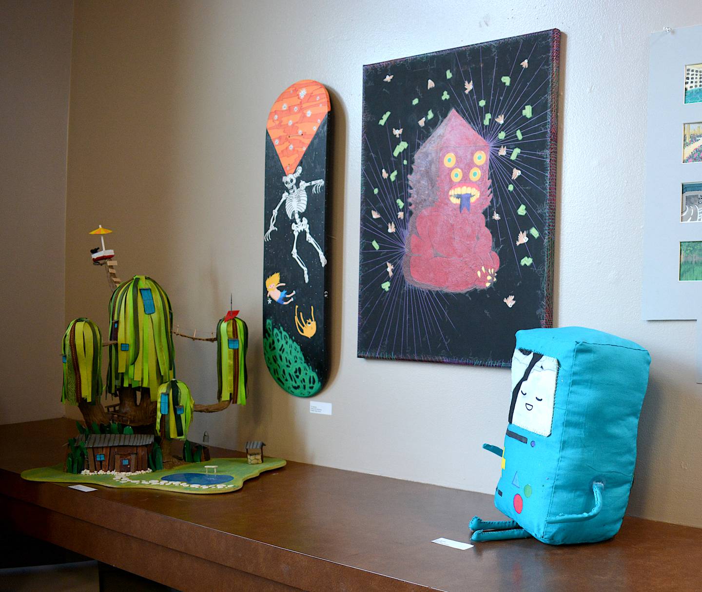 A collection of various art pieces made by CC Zachary based on imagery in cartoon series "Adventure Time." A skateboard deck shows what participants could expect from the "Art On Deck" program.