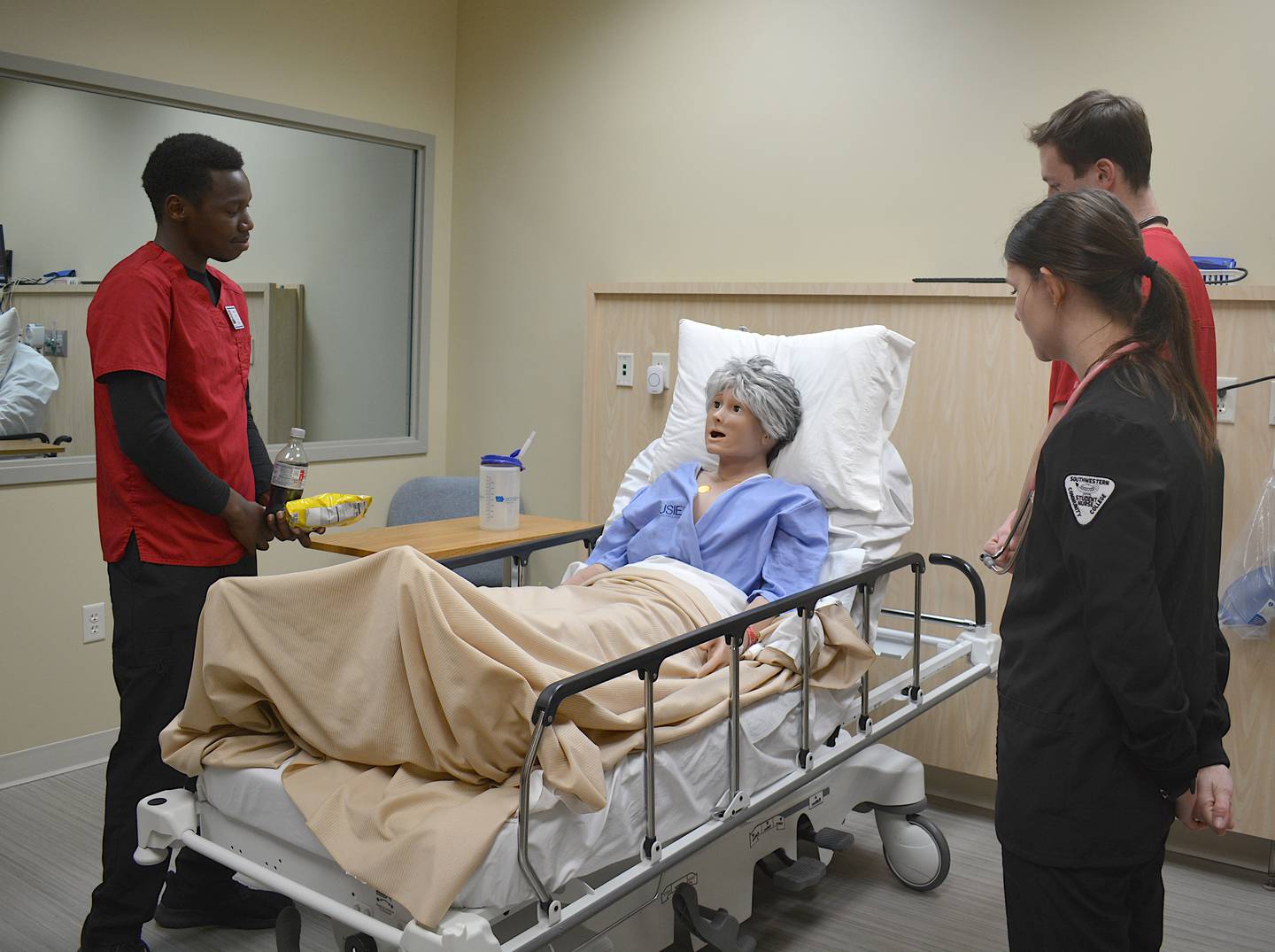 Nursing students Kevin Kiprop, left, Sophia Groumoutis, front-right, and Gavin Evans, back-right, explain to the mannequin, named Mary Jones, why they're taking away high-sodium food and drinks.