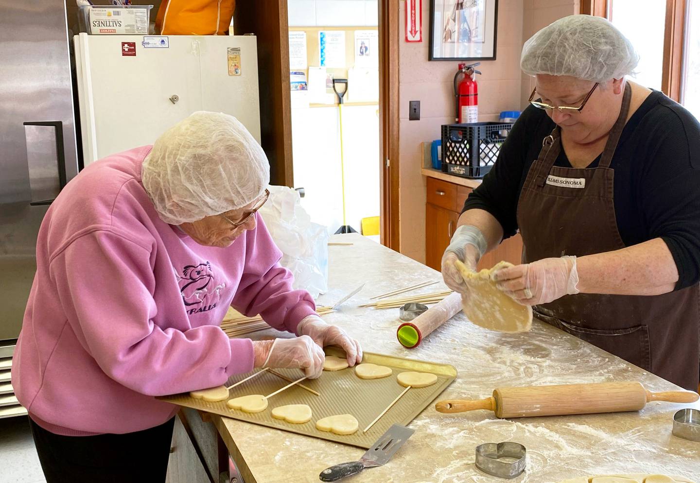 Kay Raymond, left, puts a bamboo stick into a heart-shaped cookie before it goes into the oven. On the right, Rhonda Cooper prepares dough for cookies ordered in the 2020 Valentine’s Day cookie sale. The fundraiser, originally started by Kay Ritter, is celebrating 25 years.